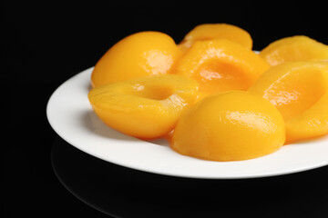 Fototapeta na wymiar Plate with canned peach halves on black background, closeup