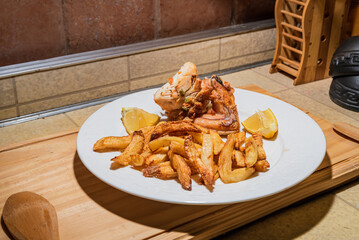 Homemade grilled chicken served on a ceramic white plate with with rustic fried potatoes and sauce. Isolated over wooden board.