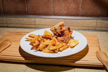 Homemade grilled chicken served on a ceramic white plate with with rustic fried potatoes and sauce. Isolated over wooden board.