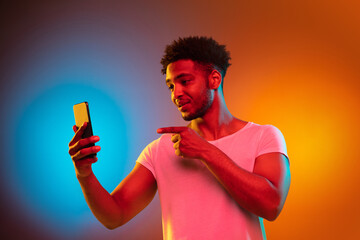 Recording voice message. African-american man's modern portrait on studio background in neon....