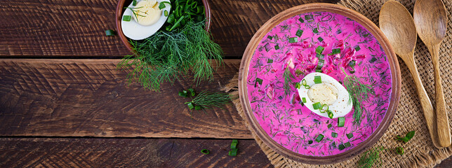Cold borscht, summer beet soup with fresh cucumber,  boiled egg and baked potatoes on wooden table....