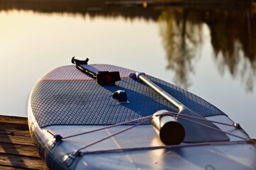 Paddleboard with a paddle on a wooden pier in the lights of sunset on a forest lake background...