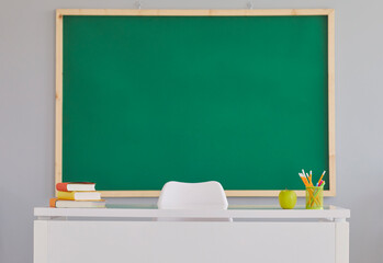 Back To School background with a clean green school board. Indoor shot of a teacher's desk and a...