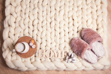 Home slippers made of fur, cup of cappuccino and inscription Home on blanket of thick yarn