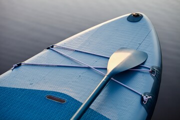 Paddleboard and surf board with paddle on blue water surface background close up. Surfing and SUP...
