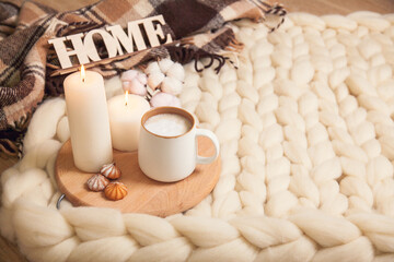Cup of cappuccino and cookies, candles, checkered plaid, inscription Home on the background of blanket of thick yarn.