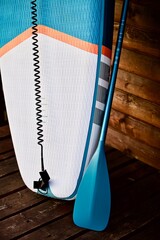 Obraz premium Paddleboard and surfboard with paddle on brown wooden wall background close up. Surfing and SUP boarding equipment in sunset lights close-up. Outdoor water sports. Surfing lifestyle backgrounds.