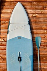 Paddleboard and surfboard with paddle on brown wooden wall background close up. Surfing and SUP...