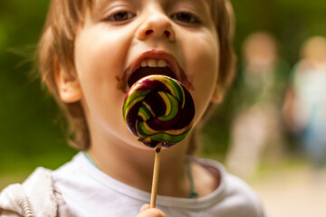 Portrait of a cute little boy holding a large round lollipop. The baby eats a sweet, big lollipop.