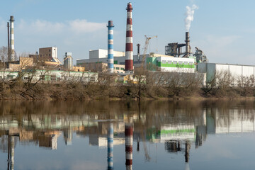 Industrial landscape. A large factory with pipes is reflected in the clear river water against the blue sky. Toxic smoke is coming from the factory's chimney. Environmental pollution