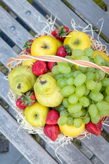 Round wicker basket full of fresh fruits and berries stands on a wooden bench top view
