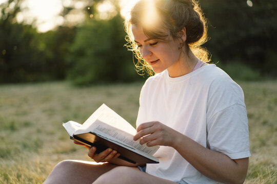 Christian woman holds bible in her hands. Reading the Holy Bible in a field during beautiful sunset. Concept for faith, spirituality and religion