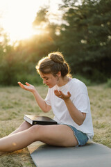 Woman closed her eyes, praying in a field during beautiful sunset. Hands folded in prayer concept...