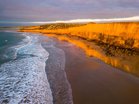 Looking down on waves breaking on a beach below coastal cliffs