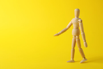 Wooden human model on yellow background, space for text. Mini mannequin