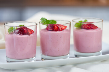 Strawberry dessert of milk and berries decomposed into cups on a wooden table decorated with fresh strawberries and mint leafs