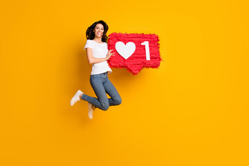 Full length body size view of lovely cheerful girl jumping holding red like board isolated over bright yellow color background