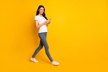 Fototapeta na wymiar Full length body size of attractive cheerful wavy-haired girl going using device gadget isolated over bright yellow color background