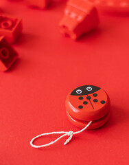 Wooden toy yo-yo in the form of a red ladybug on a red background among scattered building blocks