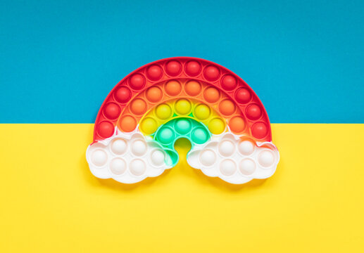 Multicolored silicone toy antistress pop it in the shape of a rainbow with clouds on a yellow blue background