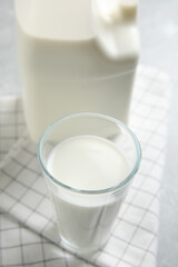 Glass of milk near gallon bottle on light table, closeup