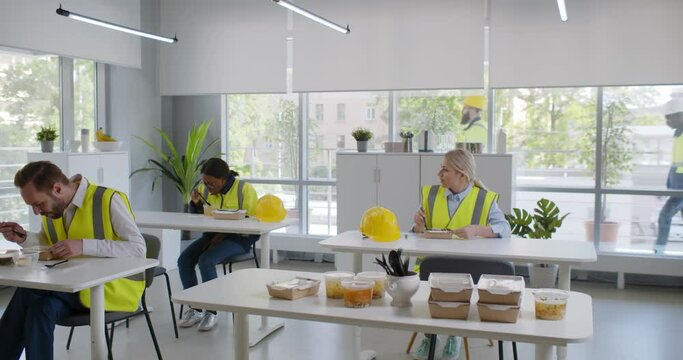 Group of technicians in factory canteen eating during lunch break and resting from work