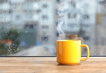Cup of hot drink near window on rainy day. Space for text