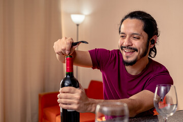 Young latin man opening a red wine bottle at home in the living room