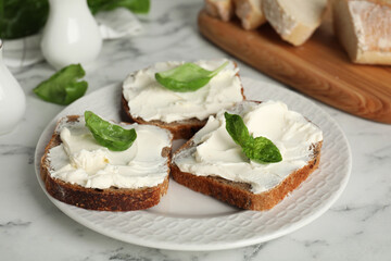 Bread with cream cheese and basil on white marble table