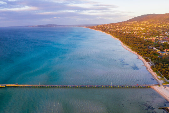 Aerial view of a long narrow jetty coming off a beach at sunset