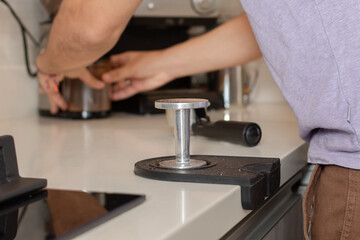 Fototapeta na wymiar Close-up and focus on the coffee tamper while a man's hands take the ground coffee in the background