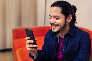 Young latin man using the phone at home in the living room