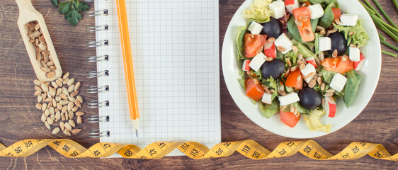 Fresh greek salad with feta cheese and notepad with tape measure. Slimming and healthy nutrition