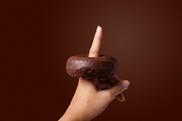 female hand with a chocolate donut on her finger with brown background