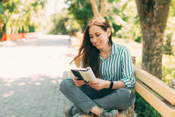 Photo of young woman reading and enjoying a book on the bench in public park.