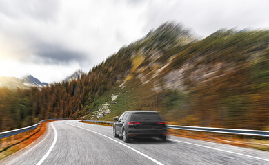 A black car rushes along the road against the backdrop of a beautiful landscape.