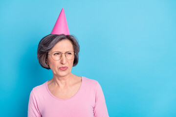 Photo of unhappy upset sad mature woman look copyspace in disgust wear cone hat isolated on blue...