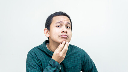 A portrait of young Asian Malay man holding chin checking his face for skin care and beauty concepts, studio shot isolated white background with copy space.