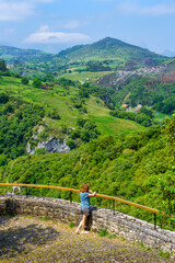 Fototapeta na wymiar Woman leaning out of a viewpoint contemplating the green landscape of the valley. Santander.