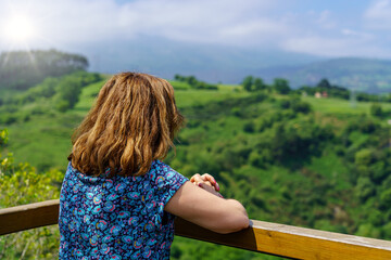 Woman contemplating the green valley from a viewpoint with flashes of the sun on the horizon....