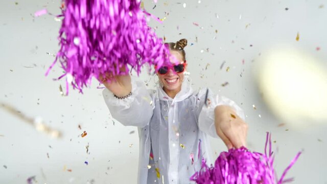 A smiling girl with red glasses shakes pompoms under falling confetti. Winning, winning, euphoria