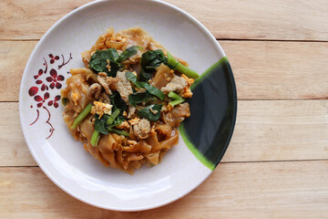 Stir-fried rice noodles, soy sauce with pork and kale in the dish, Thai delicious food isolated on wooden background closeup.
