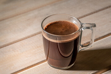 Mug of coffee on the old wooden table under the rays of the morning sun.