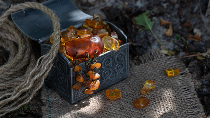 Fototapeta na wymiar Beautiful old Baltic amber brooch lies in a metal carved chest on sparkling amber stones. The composition was created on a linen fabric on the forest floor.