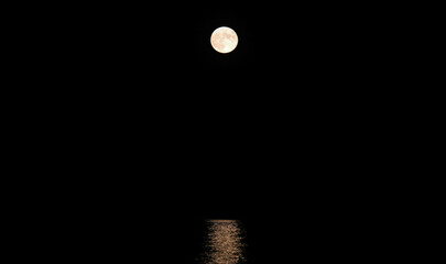 giant moon very bright and reflected to be on the placid water of the sea at midnight