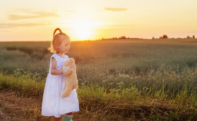 little girl with teddy bear on road at sunset