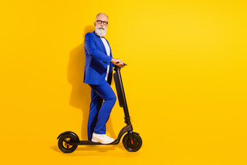 Full length body size profile side view of elegant funky man riding eco kick scooter isolated over bright yellow color background © deagreez