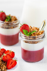 Yogurt with strawberry puree and granola in glass jars. Dessert.