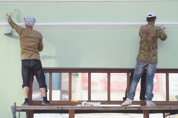 Photo of the process of painting the facade of a historical building. Roller and brush work. The workers demonstrate inspiration and a creative approach to the task.