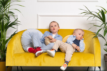 Two brothers sitting together on a yellow sofa  and making funny faces - blonde caucasian boys...